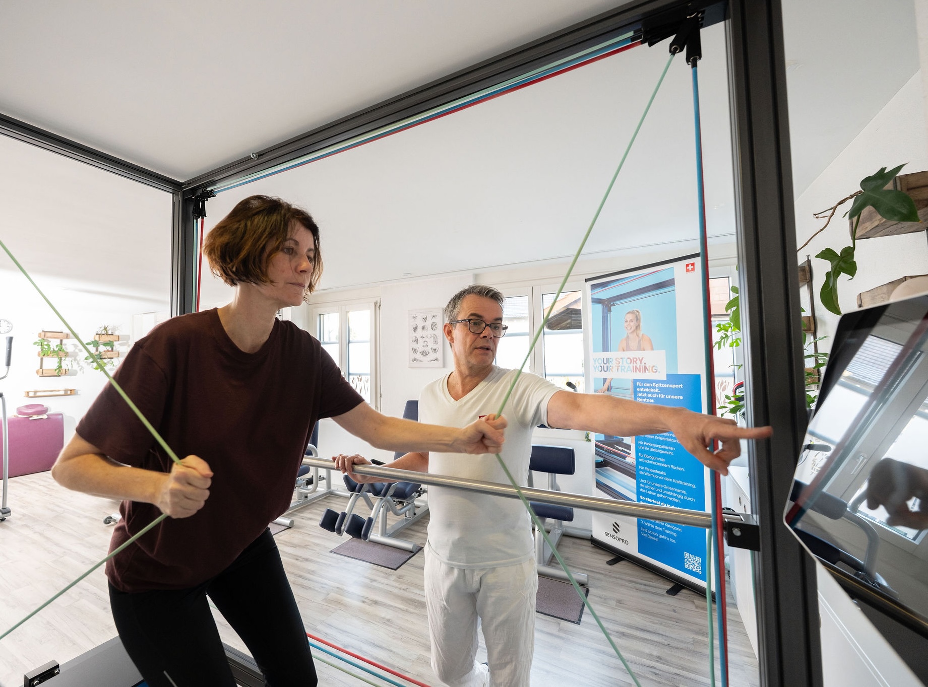 Physiotherapeut Manolito van Haren betreut Patientin beim Training mit Seilen auf dem SENSOPRO Gerät in Physio Kinetic Fehraltorf